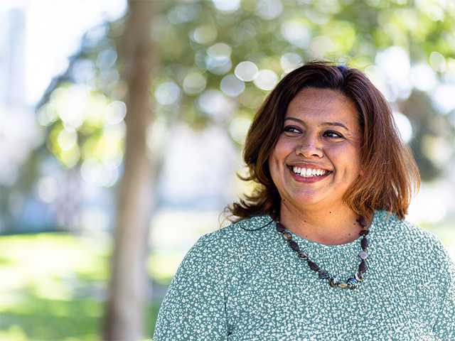 Smiling Black woman stands in the shade of trees outdoors