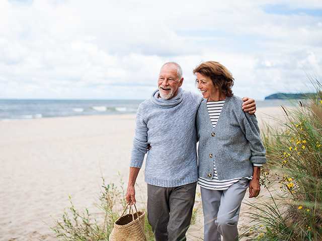 Older man and woman walk side-by-side in sand along a beach