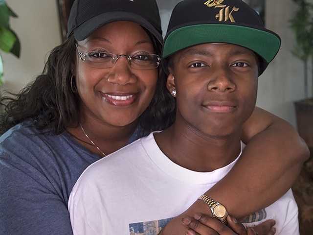 Smiling Black woman hugs her son from behind