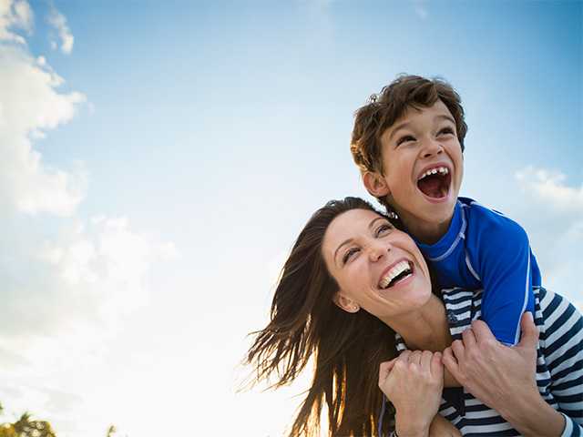 Smiling mother with laughing young son on her back in the sunshine