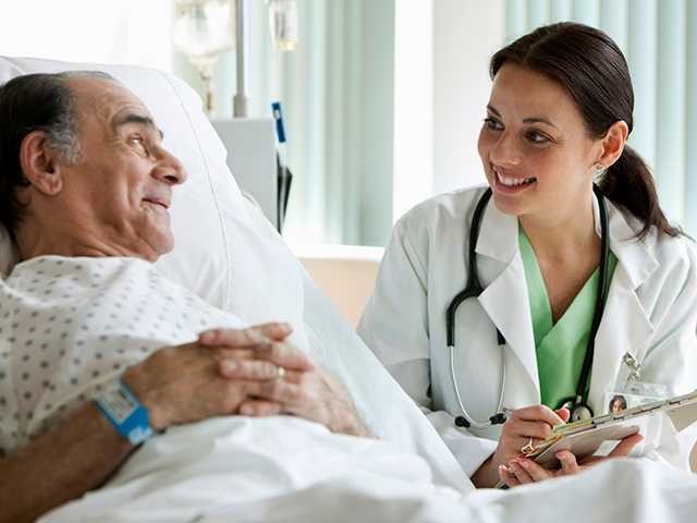 Female physician speaks with senior male patient resting in hospital bed