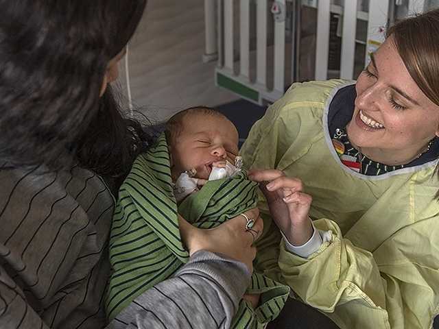 Mother holds a baby while smiling doctor reaches out in the neuromuscular clinic