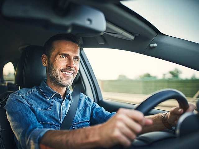 Smiling man in a blue shirt looks ahead while driving a vehicle