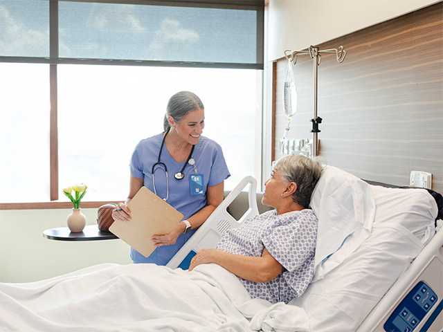 Hospital worker standing at the bedside of a patient and talking
