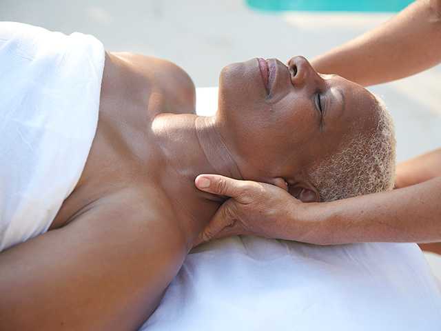 Smiling Black woman lies on her back while having her neck massaged