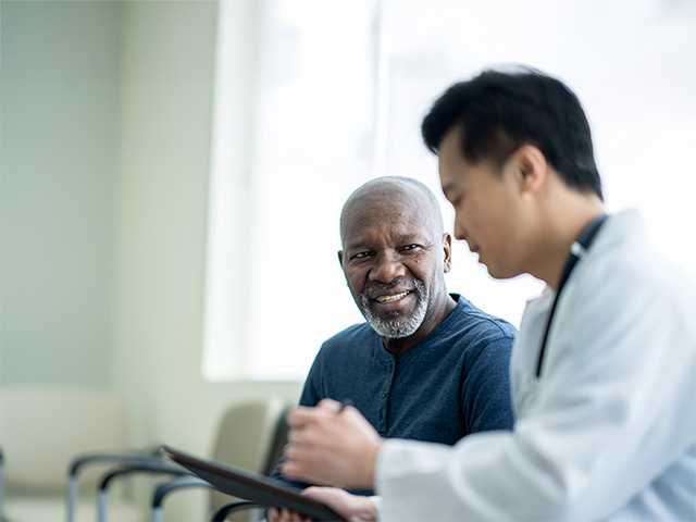 Smiling Black man wearing a navy blue shirt speaks with a Corewell Health doctor