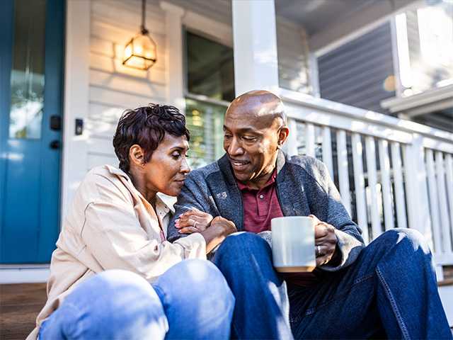 Elderly Black man sits next to his wife on the front step of their house