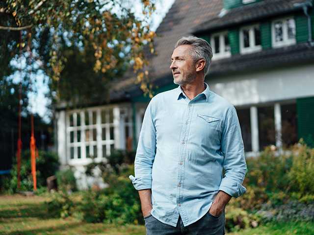 Older white man stands in front of a house in the afternoon