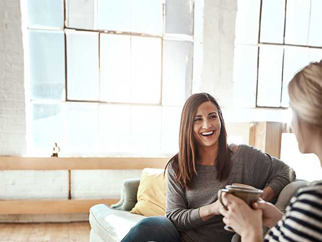 Smiling young woman with brown hair sits on couch with a mug of coffee