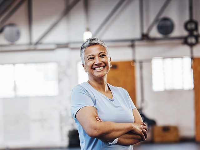 Smiling middle aged woman with short hair crosses her arms while standing in a gym