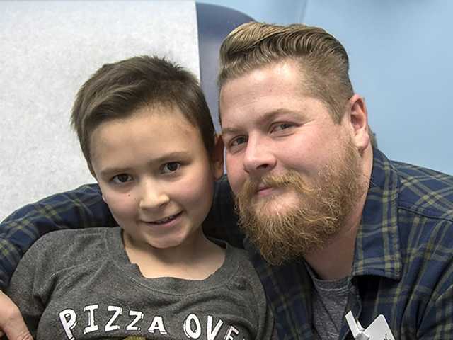 Smiling father with a beard and plaid shirt hugging his smiling son