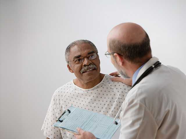 Black man with glasses speaks with a Corewell Health cancer care specialist in an exam room