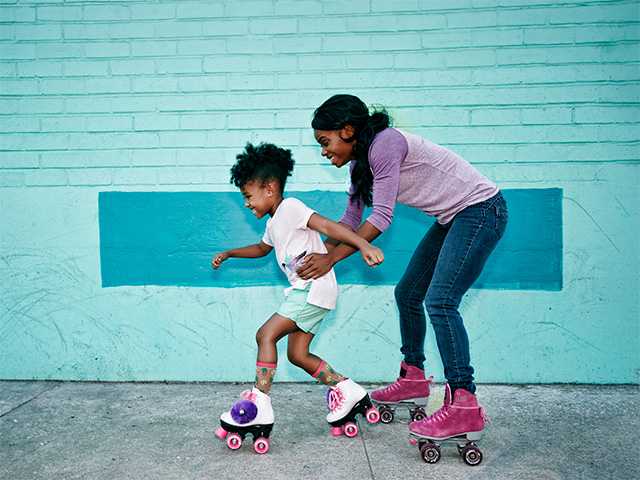 Two African American girls roller skating together in front of a brick wall