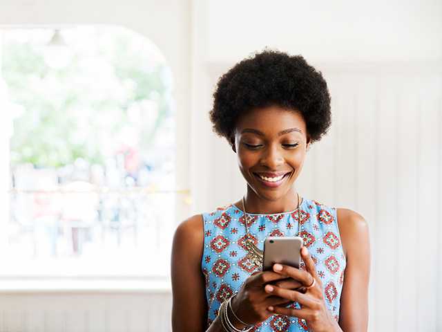 women smiling while holding her phone scheduling a doctors appointment