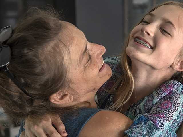 Smiling woman hugs smiling preteen girl