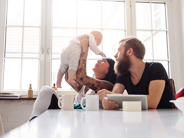 Young mother and father sit in a sunlit room as the mother lifts their baby up