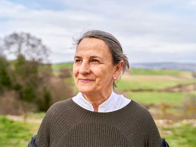 White woman with hair pulled back into a bun stands in a field outdoors