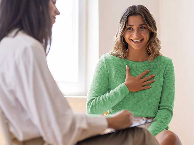 Smiling young woman in a green shirt sits next to and speaks with a naturopathic medicine provider