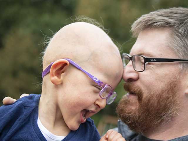 Smiling father with a beard and glasses holds his smiling daughter