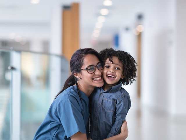 Woman in blue scrubs hugging a child in a hospital hallway