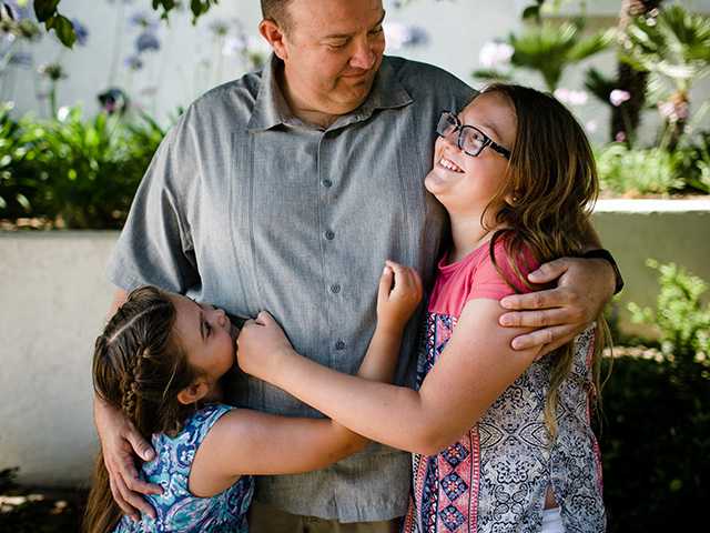 Father hugging both his daughters while they are all smiling at each other.