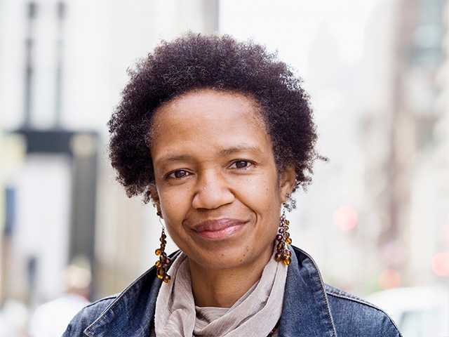 Black woman with short curly hair stands outdoors wearing a denim jacket
