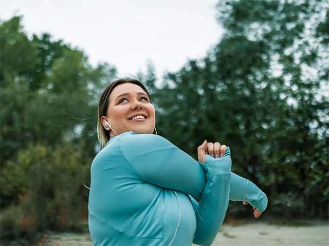 Woman in teal jacket stretches her arms