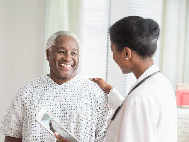 Smiling Black man wearing a medical gown speaks to his Corewell Health heart and vascular specialist