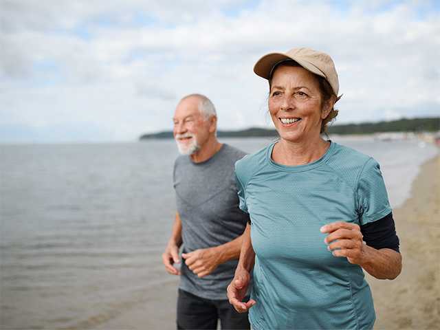 Older man and woman jogging on beach alongside a lake