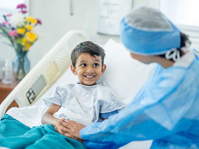 Young boy in hospital bed smiling at member of his care team before surgery.