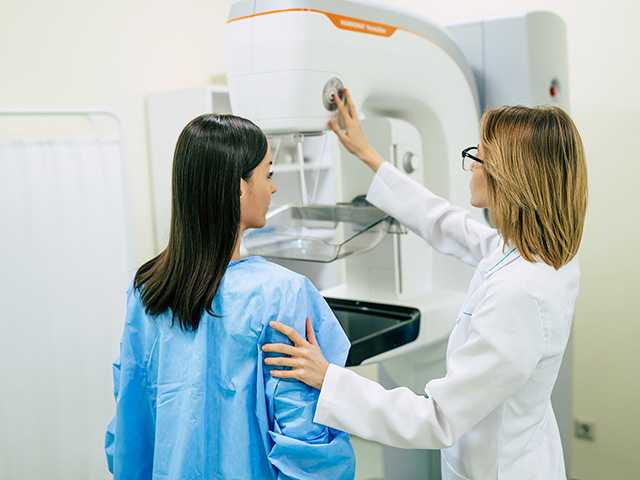Corewell Health breast imaging specialist assists a patient as she stands in front of a mammography system