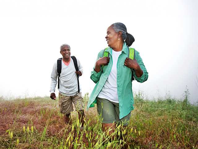 Older Black man and woman hike together through a field