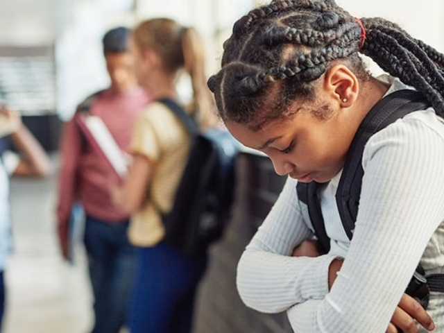Young dark haired girl looking down with a group of peers in the background.