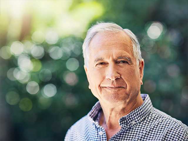 Elderly white man stands in the sunshine near trees