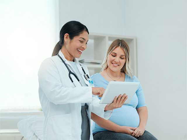 Smiling Corewell Health maternal-fetal medicine specialist speaks with her patient in an exam room