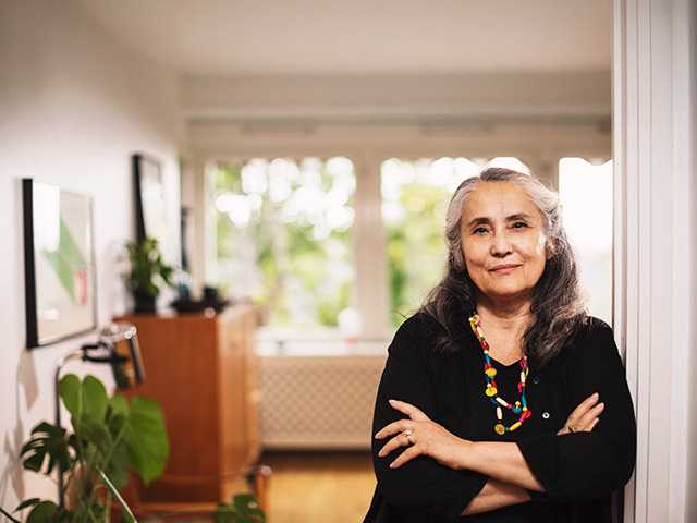 White woman wearing a black blouse leans against a wall crossing her arms