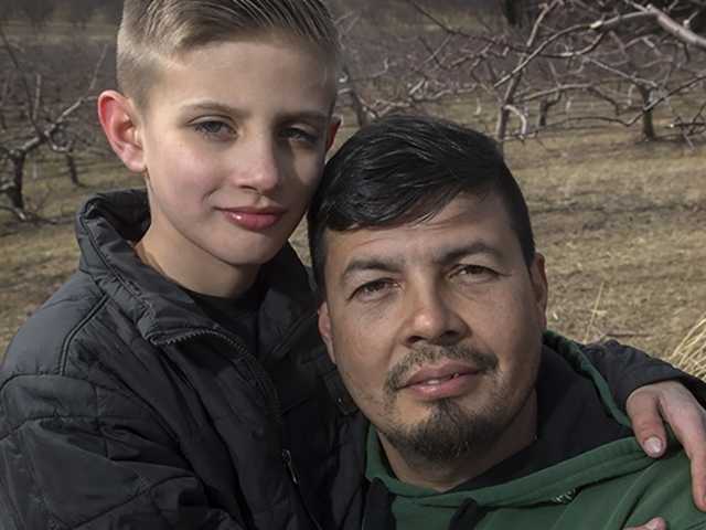 Preteen son stands next to his father in front of trees in the autumn