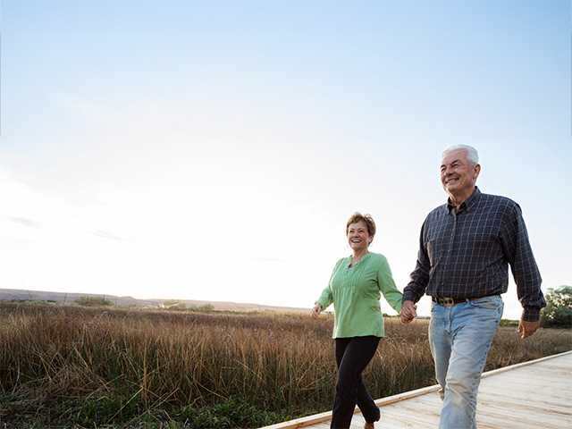 Smiling man and woman hold hands and walk along a boardwalk during a sunset