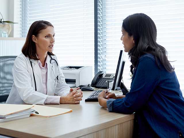 Middle aged woman in a navy blue sweater sits across a desk from a Corewell Health doctor as they discuss a second option on her condition