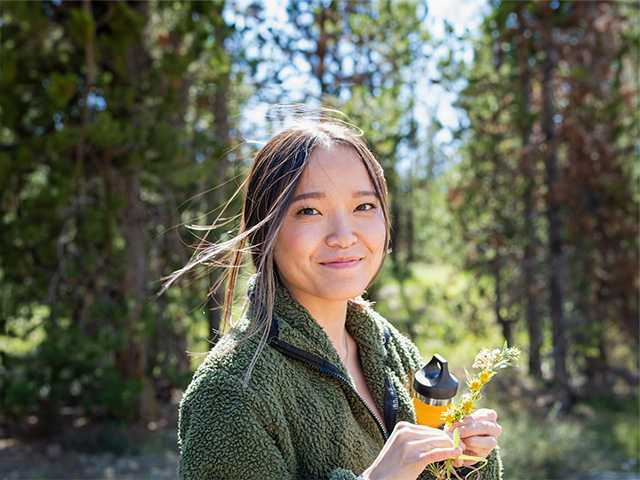 Smiling Asian woman stands in forest with a flower in her hands