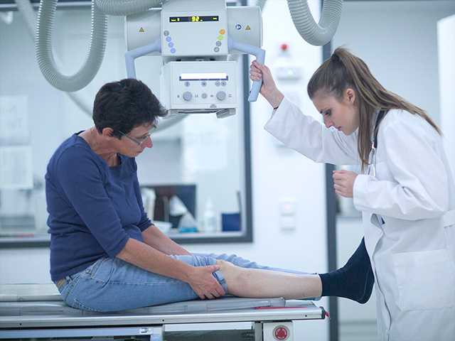 Corewell Health imaging specialist positions an X-ray machine over the leg of a patient