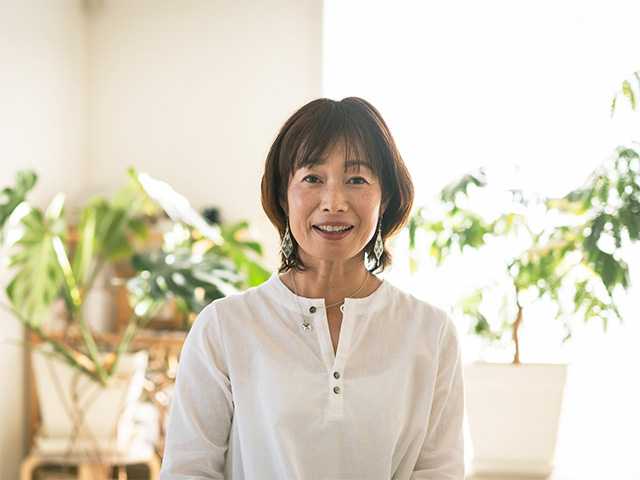 Asian woman with shoulder length brown hair stands inside a sunny room