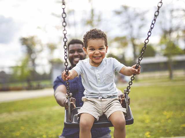 Father pushing his young son on a swing set at the park.