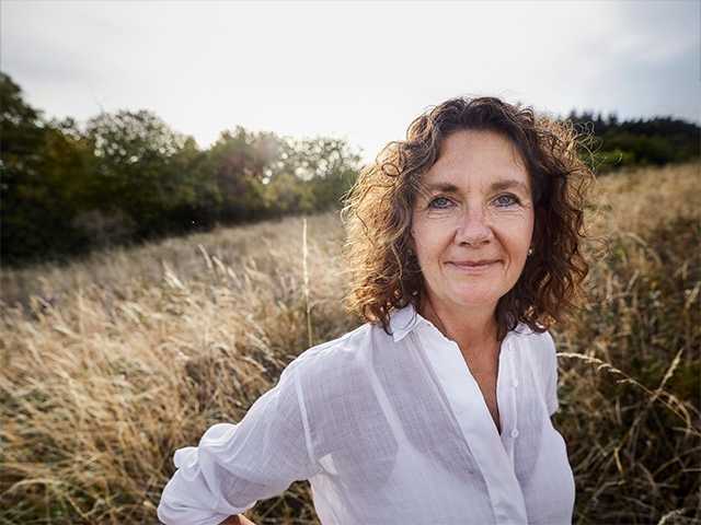 Older white woman stands in a field of wild grasses in the evening sun