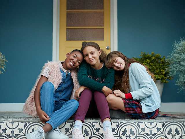 Three young teen girls sitting outside hanging out together.