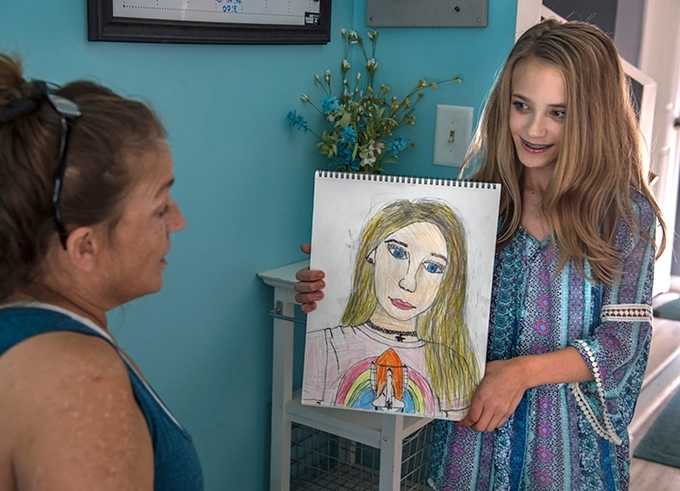 Preteen girl shows off self portrait drawing