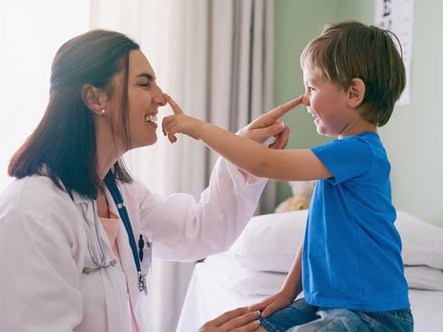 Smiling boy in a blue shirt and smiling doctor in a lab coat touch each other's noses in the pediatric vascular anomalies clinic