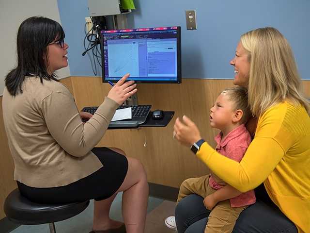 Mother sits with son on her lap, speaking with doctor in the epilepsy clinic