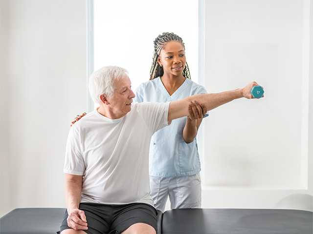 Corewell Health neuro rehab specialist helps an elderly man stretch his arm while holding a weight