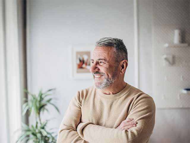 Smiling white man wearing a sweater crosses his arms while looking out a window